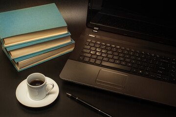 A cup of coffee near the computer, books and a pen on a black background