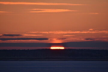 Sunrise over a frozen snow covered lake. Part of sun visible behind clouds