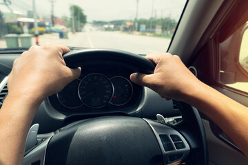 Two arm turns the steering wheel of a car. Blurred of the road cleared in the daytime.