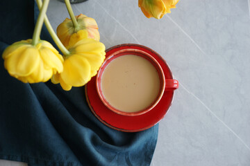 Bouquet of yellow tulips in a vase and a red cup with coffee on a gray table