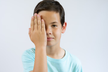 Little caucasian boy kid wearing casual clothes covering one eye with hand