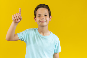 Photo of young Boy funny holding up index finger pointing up at something. colorful yellow background.