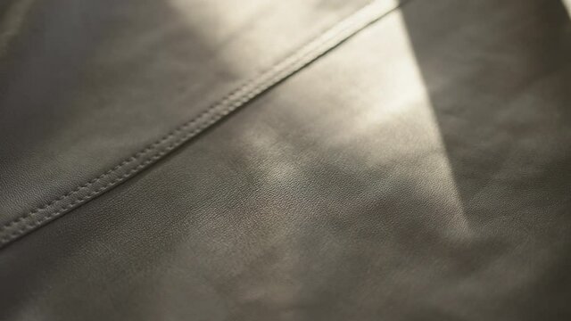 Slow motion handheld shot of soft gray leather with seam under warm sun light