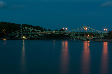 Obraz premium Long exposure landscape of old, green metal bridge at night. Smooth blue water.