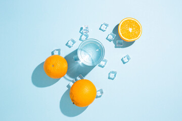 oranges, a glass of water and ice cubes on a table on a blue background. Top view, flat lay
