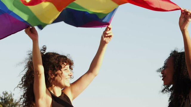Two multiethnic women celebrate gay pride with a lgtb flag in a demonstration
