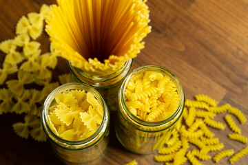 Close up of different kinds of pasta in jars on a dark wooden plate in top view