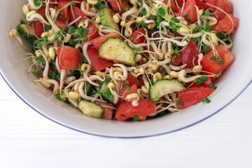 Salad with vegetables and microgreens, sprouts of cereals and broccoli, tomatoes, cucumbers, oil, salt, pepper in white bowl on light background. Healthy energetic meal. Copy space.