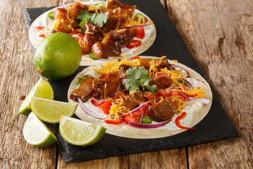 Hot tacos with grilled pork belly, seasonal vegetables, cheddar and lime close-up on a slate board on the table. horizontal