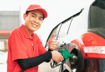 Asian gas station worker give thumbs up in one hand and holding green fuel nozzle into one hand to fill energy power fuel into black car tank, commercial service for benzine, diesel, gasohol, gasoline