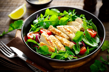 Grilled chicken breast and salad. Fresh vegetable salad with tomato, arugula, spinach and grilled chicken meat in bowl, healthy food.