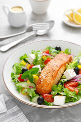 Salmon fish salad. Fresh vegetable greek salad with tomato, pepper, lettuce, olives, cucumbers, feta cheese and grilled salmon fish fillet, healthy food, omega 3, keto diet, mediterranean cusine.