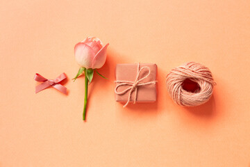 Gift box, ribbon, string, rose flower on orange background. flat lay, top view, copy space