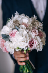the groom in a dark jacket holds a bouquet of a bride from pink and white flowers