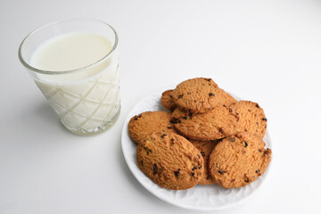 Food, baking and eating concept - close up of chocolate oatmeal cookies and milk glass on plate. Cookies and a glass with milk on white background.