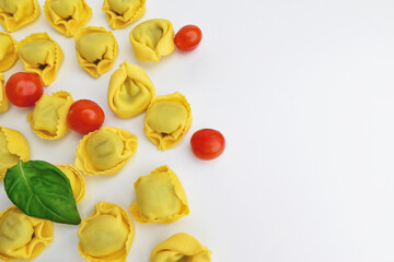 Italian stuffed pasta, tortellini, ravioli with cherry tomatoes. Tasty raw ravioli with cherry tomatoes, and basil on a light background. The process of making Italian tortellini,. Copy space.