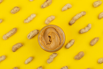 Bowl of peanut butter and scattered peanuts on yellow background