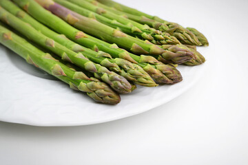 Asparagus. Green Asparagus. Bunches of green asparagus on the white plate. Green asparagus sticks isolated on white background. Space for text, copy space.
