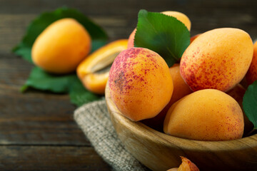 Ripe apricot with leaves in a bowl on a wooden table. Home harvest from your own garden.