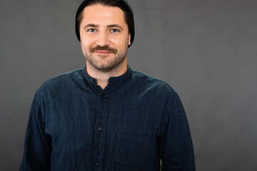 Obraz premium Young hipster guy in knitted hat and casual wear looks at camera with smile isolated on dark background. Concept of self-confident, opportunities, career growth, business education, success, freelance