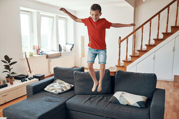 Happy boy jumping on sofa and smiling while having fun at home