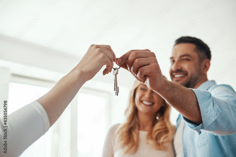 Wall mural young beautiful couple in casual wear smiling while receiving keys from new home