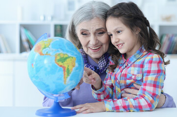 Fototapeta premium Smiling grandmother and granddaughter sitting at table with globe