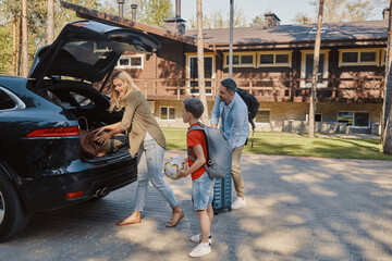 Happy family packing stuff in car and smiling while standing in front of the house