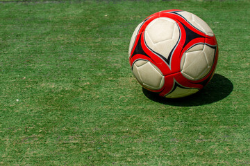 Fototapeta na wymiar Red and white soccer ball on bright green grass in the sunshine on a summer day for children's recreation.