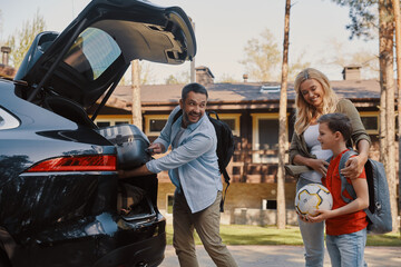 Happy family packing stuff in car and smiling while standing in front of the house