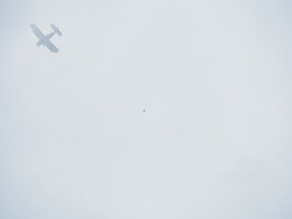 In the gray cloudy sky, an airplane and a parachutist