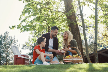 Happy young mother and father with little boy smiling while having picnic outdoors