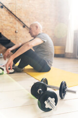 Fototapeta na wymiar Dumbbells and elderly man relaxing after his fitness workout at home