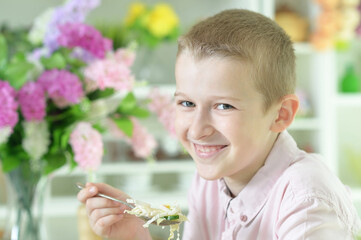 Cute boy preparing salad on kitchen table at home