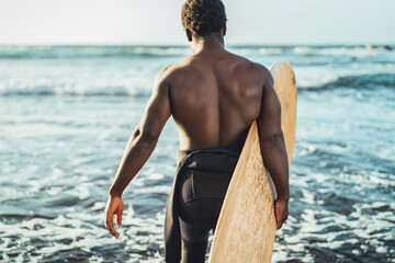 Afro surfer having fun surfing during sunset time - African man enjoying surf day - Extreme sport lifestyle people concept