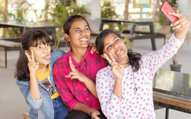 Focus on last girl, Young teenager girls with grimacing taking selfie at restaurant - girls having fun by taking photos on mobile phone - Concept best friends and youth culture