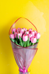 Bouquet of pink tulips in a vase on a yellow background.