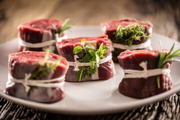 Raw beef steak cuts on a plate wrapped with strings and fresh herbs