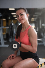 Fototapeta na wymiar Cheerful female weightlifter exercising with dumbbells at the gym