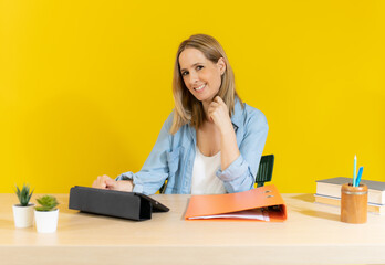 Smiling young woman using laptop looking at camera over yellow background