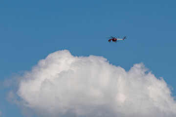 Fototapeta na wymiar A large red and white fire brigade helicopter flies in the sky above a cloud for a fire rescue