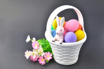 Several colored Easter eggs are on a white basket with a bunny inside on black background.