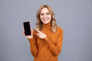 Woman point finger at blank mobile phone screen grey background copy space, advertising smartphone.