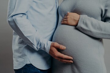 Cropped shot of unrecognizable woman and man expect baby. Pregnant wife pose with husband indoor. Future parents prepare for child birth