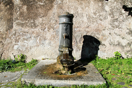 Typical drinking water fountain called "nasone" in Rome, in the background an old flayed wall and uncultivated herbs.