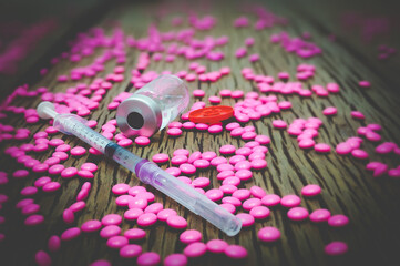 Syring for a colored injection with a needle inserted. There is a water pill inside There was a bottle next to it. There are pink pills on a brown plank concept, drug addiction.