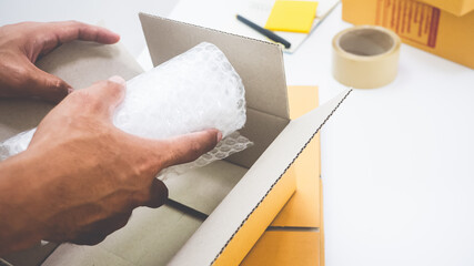 Transparent parcel wrapping sheet Package Putting stuff in a brown parcel box With a man's hand on it Besides, there is masking tape, notepad, concept selling online, delivery, covid-19