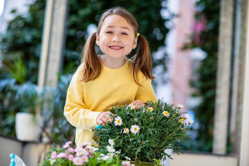 Happy little girl caring for balcony flowers, pruning with pruning shears