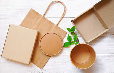Top view of Paper box packaging in rectangle and round shape and paper bag with green leaves on white wooden background , delivery eco package and save environment  concept