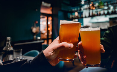 Closeup view of a two glass of beer in hand. Beer glasses clinking in bar or pub